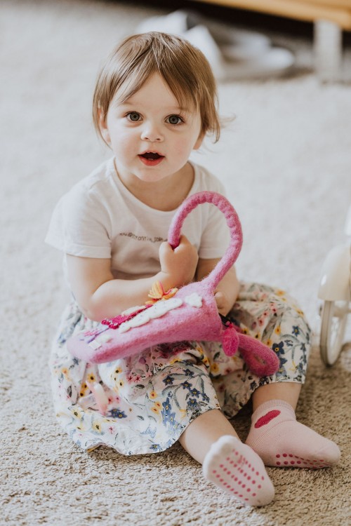 Ein kleines Mädchen sitzt auf dem Boden mit ihrer pinken Tasche.