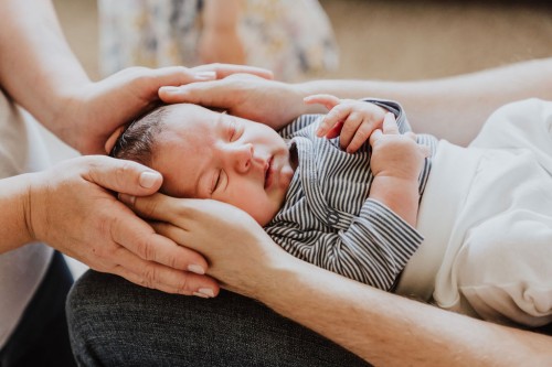 Ein kleines Baby wird von großen Händen festgehalten.