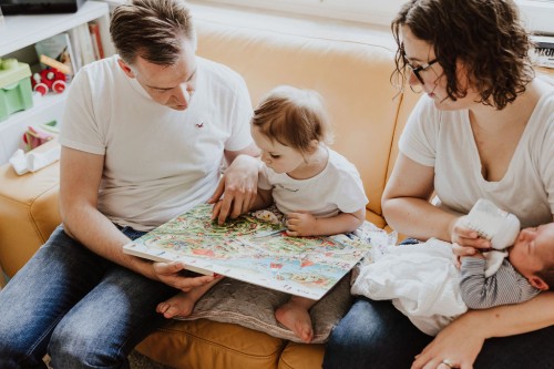 Eine Frau und ein Mann sitzen auf einer Couch und lesen einem Mädchen ein Buch vor.