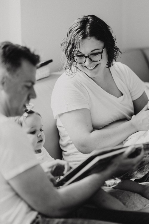 Eine Frau und ein Mann sitzen auf einer Couch und lesen einem Mädchen ein Buch vor.