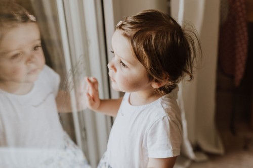 Ein kleines Mädchen schaut durch ein Fenster.