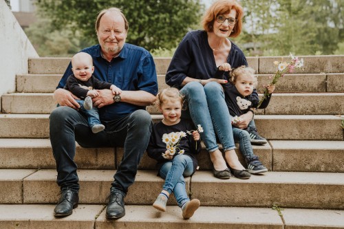 Oma und Opa posieren mit ihren Enkel:innen sitzend auf der Treppe