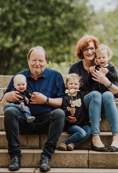Oma und Opa posieren mit ihren Enkel:innen sitzend auf der Treppe