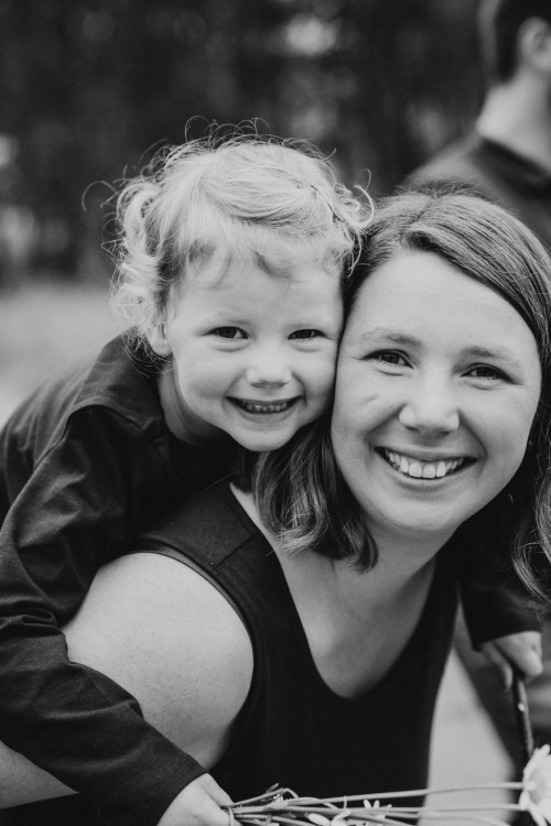 Ein kleines Mädchen kuschelt sich an Mamas Rücken und beide lächeln für das Familienbild