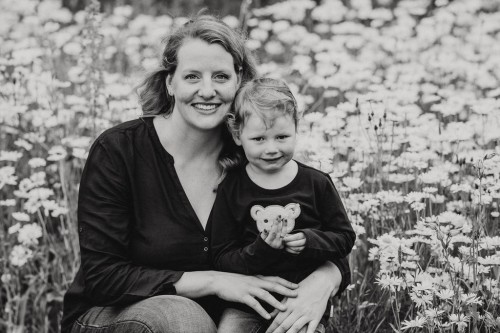Ein Mutter - Tochter Portrait die im Blumenfeld sitzen und in die Kamera lächeln.