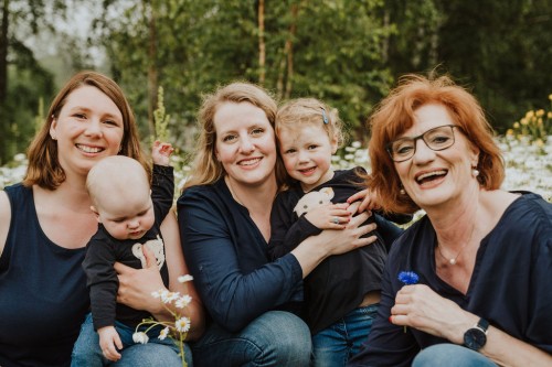 Drei Generationen von Frauen auf einem Foto, sie schauen in die Kamera und lächeln fröhlich.