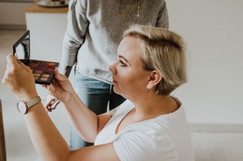 Eine Frau schaut in den Spiegel einer Lidschatten-Palette.