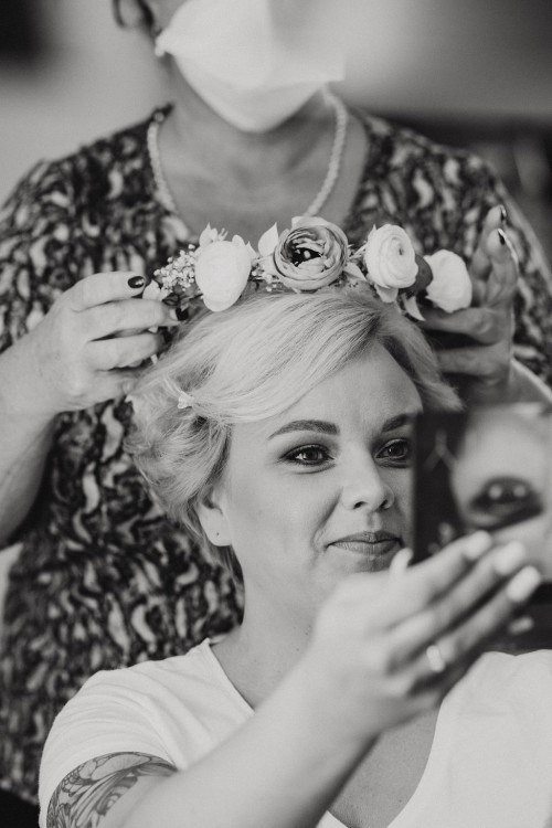 Ein schwarz-weißes Bild von einer Frau die einen Blumenkranz auf den Kopf gelegt wird.