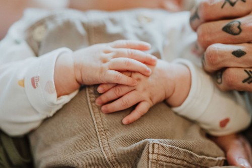 Kleine Baby Hände und die tätowierte Hand eines Mannes.