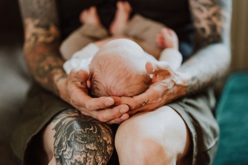Ein tätowierter Mann hält auf seinen Händen ein kleines Baby.