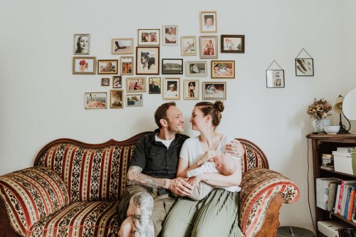 Ein Mann und eine Frau mit einem Baby auf dem Arm sitzen auf einem Sofa.