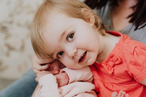 Ein kleines Mädchen kuschelt die Hände vom Baby.