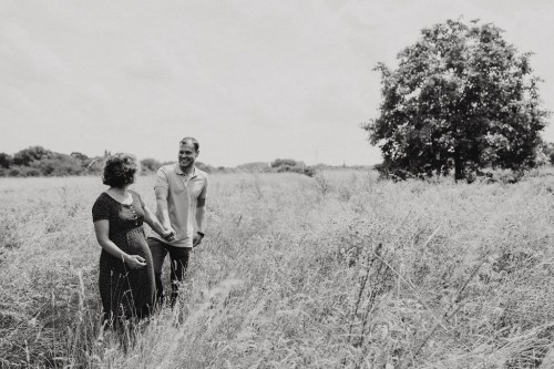 Eine schwangere Frau und ein Mann gehen händchenhaltend durch die Wiese.