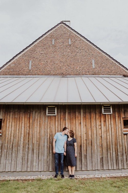 Eine Frau und ein Mann stehen vor einer Holzwand und küssen sich