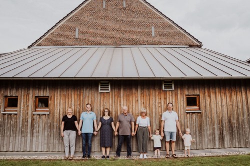 Eine Gruppe von Menschen hält Händchen und steht vor einer Holzwand.