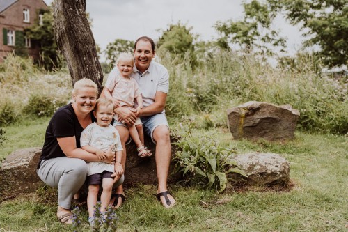 Familienfoto von Eltern mit deren kleinen Kindern sitzend in der Natur.