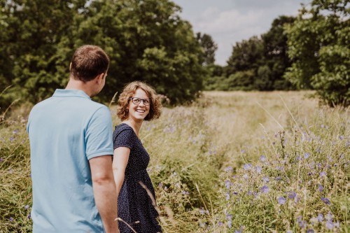 Eine schwangere Frau und ein Mann gehen händchenhaltend durch die Wiese.
