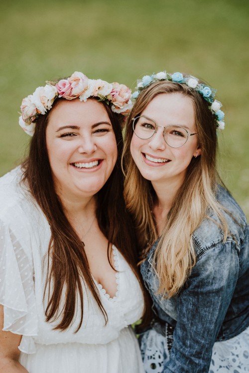 Zwei Frauen mit Blumenkranz schauen lächelnd in die Kamera.