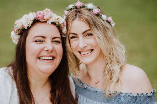 Zwei Frauen mit Blumenkranz schauen lächelnd in die Kamera.