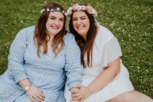 Zwei Frauen mit Blumenkranz schauen lächelnd in die Kamera.