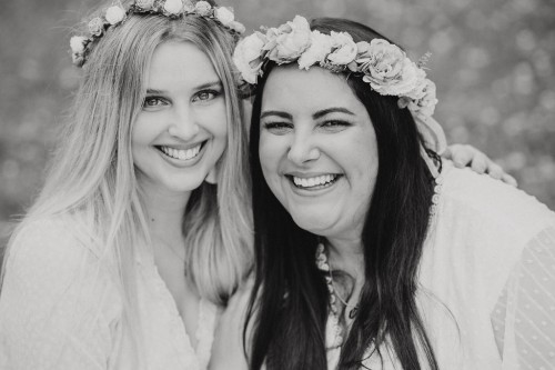 Zwei Frauen mit Blumenkranz schauen lächelnd in die Kamera.