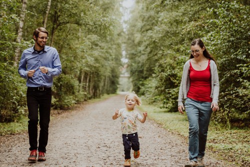 Ein Mann, eine Frau und ein Kind gehen einen Waldweg entlang.