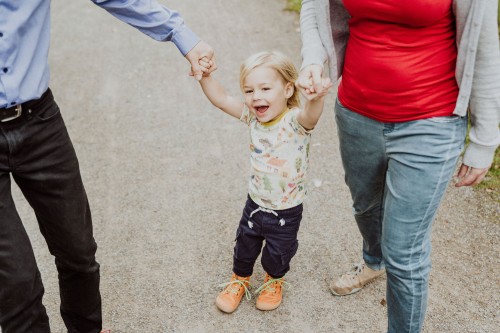 Ein kleines Kind hält Händchen mit Mama und Papa und macht Quatsch.