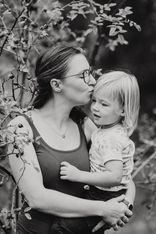 Eine Frau hält ein Kind auf dem Arm und gibt ihm ein Küsschen.