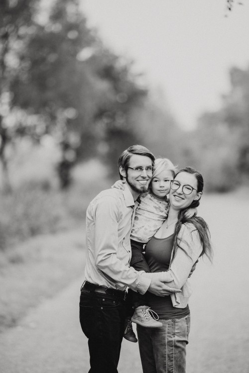 Eine Frau und ein Mann halten ein Kind auf dem Arm mitten im Wald.