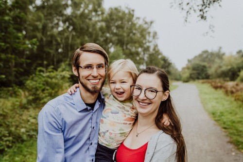 Eine Frau und ein Mann halten ein Kind hoch und lächeln.