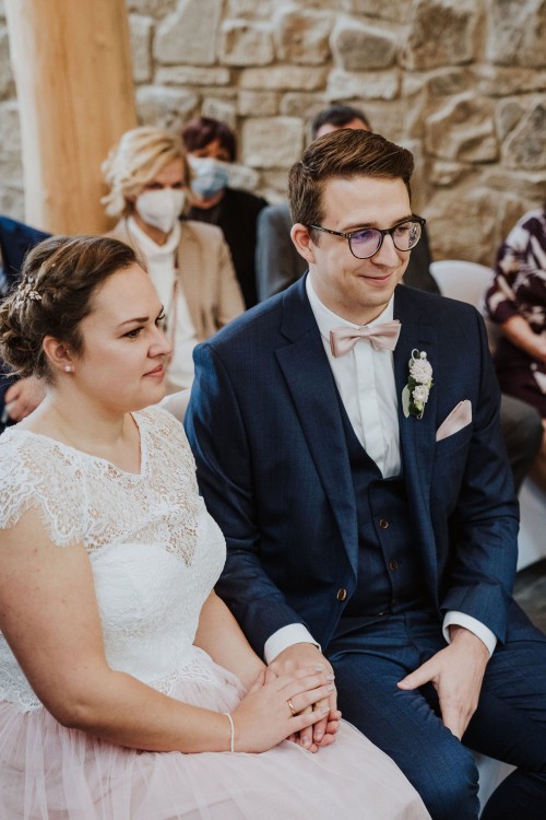 Eine Braut und ein Bräutigam sitzen nebeneinander und halten sich an den Händen.