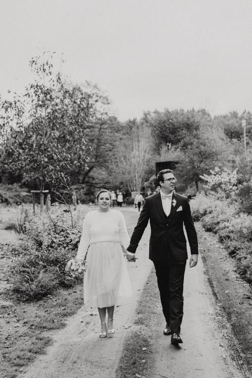 Ein schwarz-weißes Bild von einem Brautpaar das einen Feldweg entlang geht.