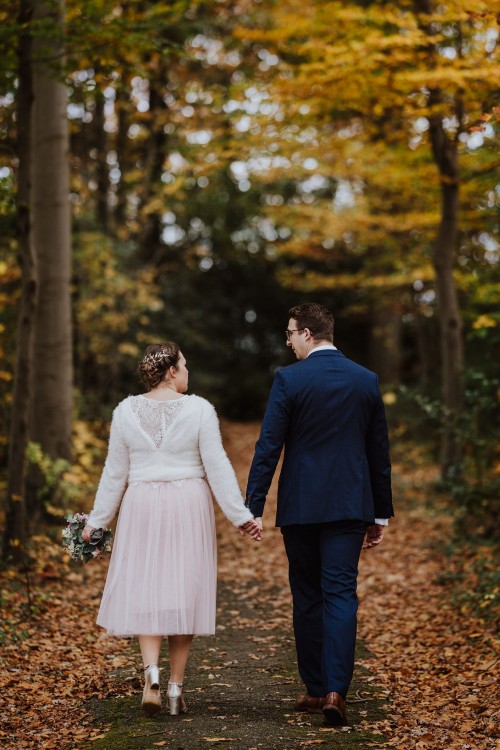 Ein Brautpaar geht händchenhaltend durch einen Wald.