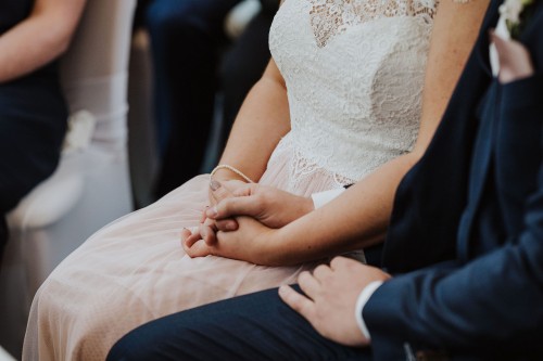 Eine Braut und ein Bräutigam sitzen nebeneinander und halten Händchen.