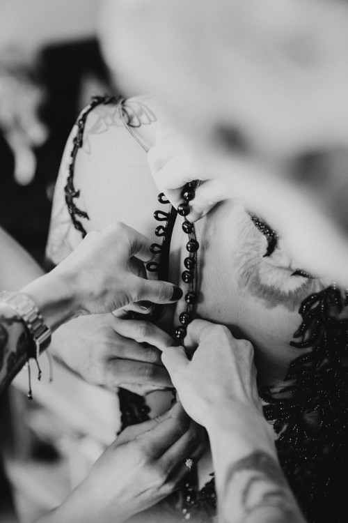 Mehrere Frauen knöpfen das Brautkleid zu.