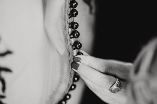 Eine Frau knöpft der Braut das Kleid zu.