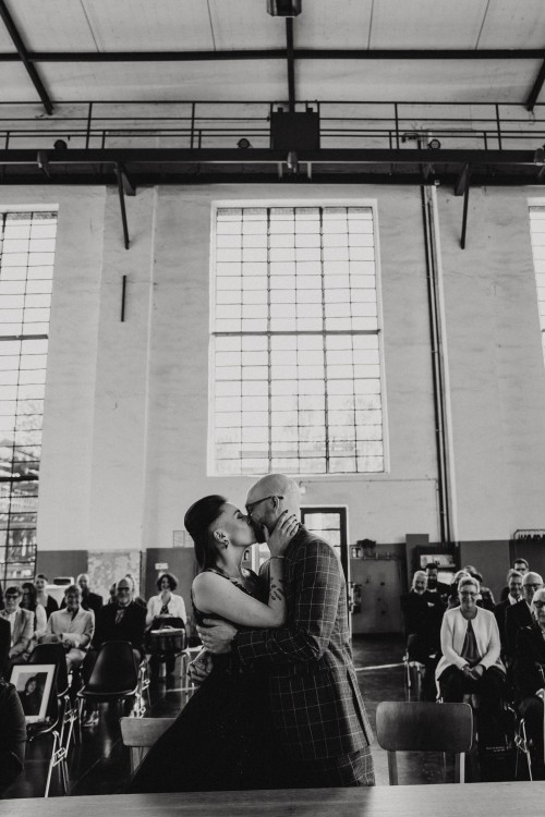Ein schwarz-weißes Bild von einem Brautpaar, dass sich küsst und die Gäste schauen zu.