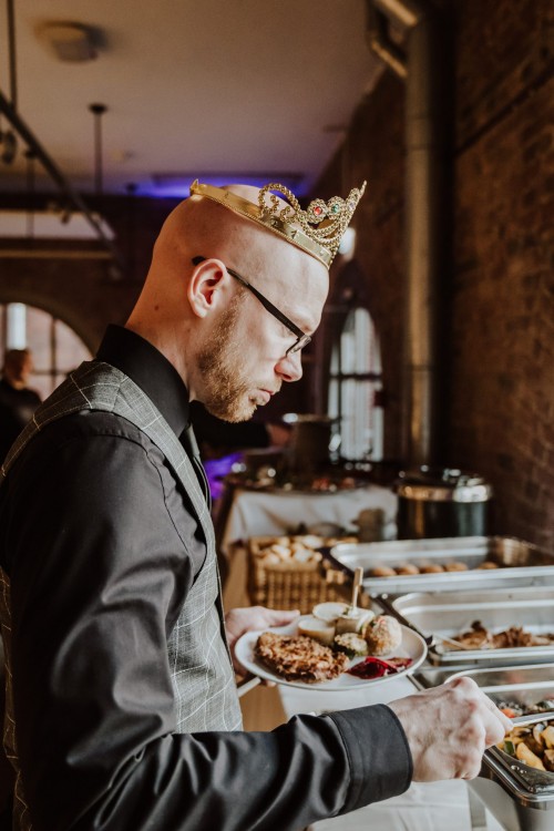 Ein Bräutigam mit Krönchen steht am Buffet.