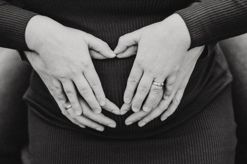 Hände von einer Frau und einem Mann auf dem Schwangerschaftsbauch.