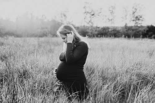 Eine schwangere Frau posiert für ein Foto auf einem Feld.