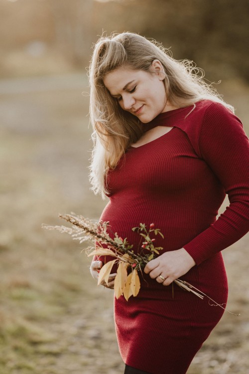 Eine schwangere Frau in einem roten Kleid mit einem Blumenstrauß.