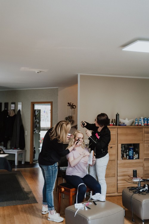 Eine Frau wird von zwei Frauen geschminkt und gestylt.