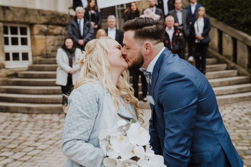 Ein Brautpaar küsst sich vor dem Rathaus Kray und die Gäste schauen im Hintergrund zu.