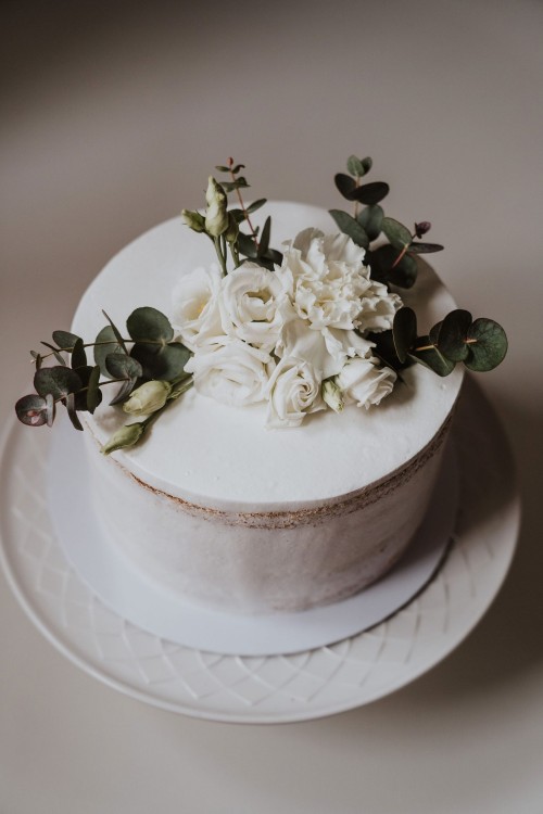 Eine weiße Torte mit Blumen und Eukalyptus drauf.