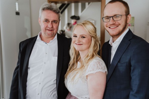 Eine Frau und zwei Männer lächeln in die Kamera.