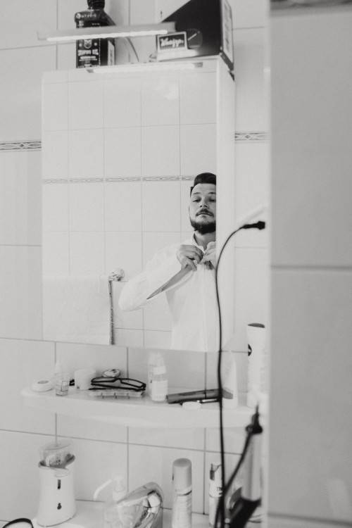 Ein Bräutigam knöpft sich das Hemd vor dem Spiegel zu.