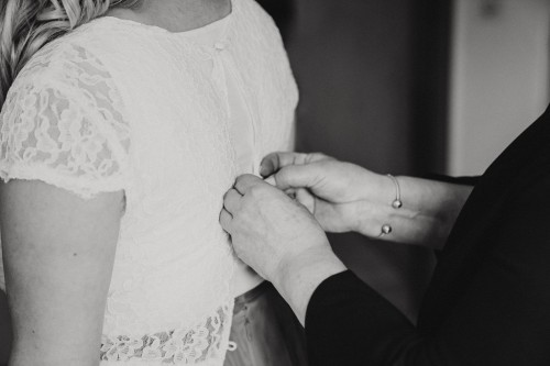 Eine Frau knöpft der Braut das Oberteil zu.