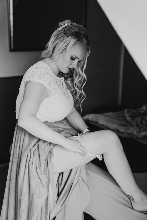 Ein schwarz-weißes Bild von einer Braut die sich das Strumpfband anzieht.