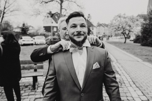 Ein Mann richtet dem Bräutigam den Kragen.