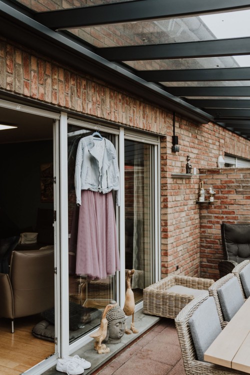 Ein Kleid und eine Jeans Jacke hängen vor dem Fenster im Wintergarten.